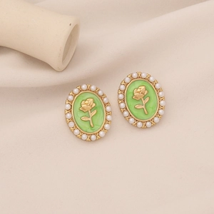 Close-up of vintage gold earrings with white pearl border and green rose relief