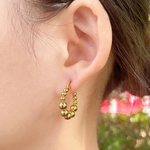 Detail shot of golden beaded hoop earrings worn on ear with soft outdoor bokeh effect
