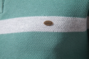Makroaufnahme von grün-weiß gestreiftem Strickstoff mit einem Logo aus Bronze