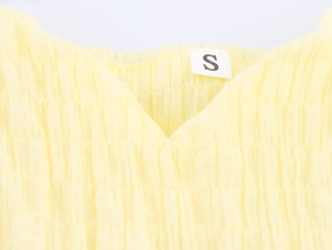 Detail of yellow crinkle fabric texture and S size label on a pleated camisole dress