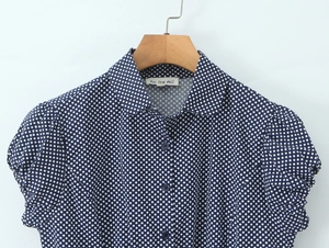 Dettaglio delle maniche a sbuffo e del colletto di una camicetta blu navy a pois