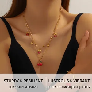 Detail of layered gold-plated necklace and bracelet featuring red cherry charms on a model