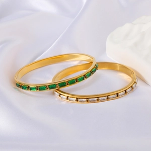 Detail of 18k gold bracelets with green emerald and clear crystals on white silk fabric