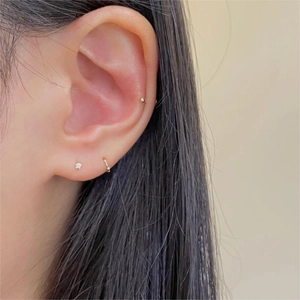 Close-up of minimalist gold hoop and stud earrings set with zircon on human ear