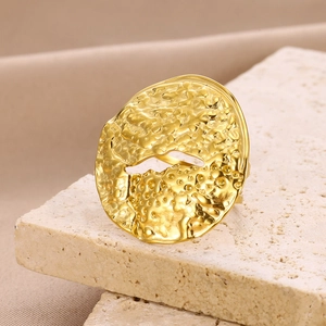 Detail of minimalist gold irregular ring with lava texture on beige stone display