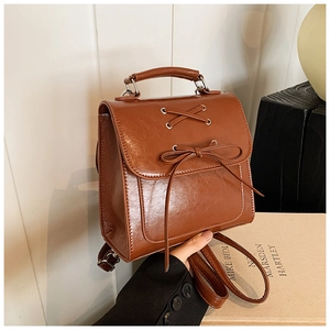 Close-up of caramel brown PU leather backpack with vintage bow and lace-up flap detail