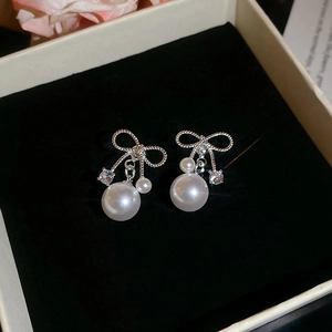 Macro shot of silver bow pearl earrings with cubic zirconia on black velvet