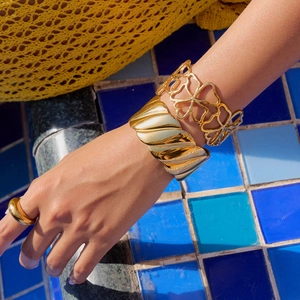 Close-up of golden wide spiral bangle and clover pattern bracelet on a female wrist