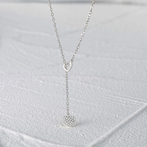 Macro detail of silver Y-shaped necklace featuring a hollow heart and sparkling zircon heart