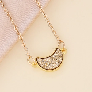 Golden crescent moon necklace with sparkling inlay on elegant beige silk fabric background