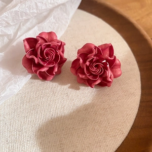 Macro detail of dark red resin rose earrings with delicate petals on linen surface