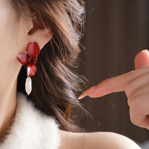 Detail of red flower earring with baroque pearl drop worn by a model in soft light