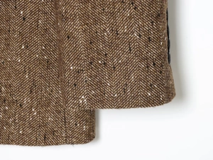 Close-up of brown herringbone wool blend fabric showing detailed texture on sleeve cuff