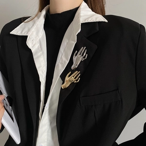Detailed view of polished gold and silver palm brooches worn on a black suit lapel