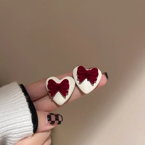 Close-up of red velvet bow and pearl heart earrings with elegant gold-tone studs
