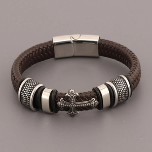 Détail d'un bracelet en cuir tressé marron avec une breloque en croix métallique