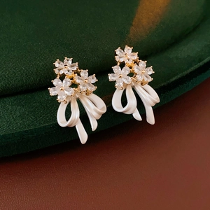 Gros plan de boucles d'oreilles fleurs dorées avec zircons et nœuds blancs élégants