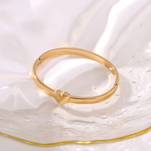 Polished 18K gold stainless steel heart cuff bracelet on elegant white silk and glass tray
