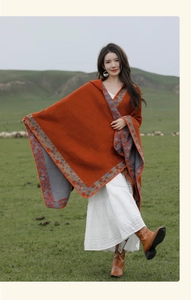 Ethnic hooded poncho in orange with floral trim worn outdoors on a scenic grassland