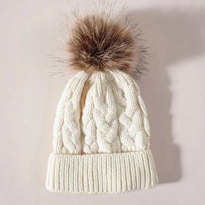 Detailed macro view of cream knit winter hat featuring chunky cable stitch and faux fur pom