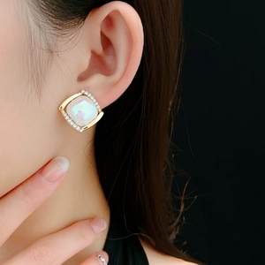 Détail de boucles d'oreilles carrées dorées avec pierre irisée et petits diamants