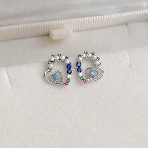 Macro shot of silver heart stud earrings with colorful gemstones and pearls in a jewelry box
