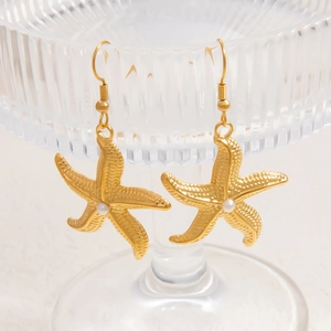 Detailed shot of 18k gold starfish earrings with white pearl inlay on glass edge