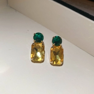 Detail of pineapple-shaped earrings with green round and yellow square crystals in gold claws