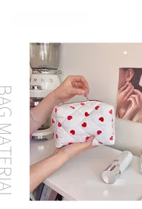 Detailed shot of white quilted heart cosmetic bag with red zipper held by hand