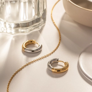 Detail of 4mm two-tone gold and silver hoop earrings with a thin gold necklace on white