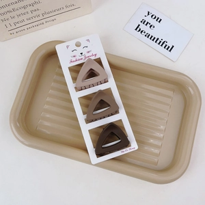 Close-up of three matte brown triangular hair clips in a stylish gift tray display