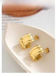 Detail shot of minimalist C-shaped gold-plated stud earrings on a stone jewelry tray