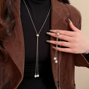 Détail d'un collier en Y minimaliste doré et argenté avec perles porté sur un blazer