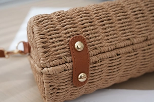 Detail view of woven straw bag bottom with brown leather trim and gold metal feet studs