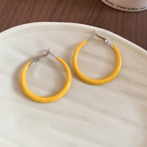 Vue de dessus de créoles géométriques jaunes avec tiges en argent sur une assiette en céramique