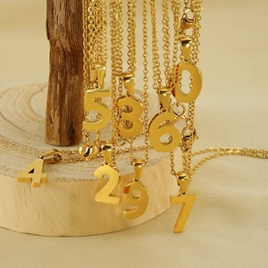 Golden 18K stainless steel number necklaces hanging on a wooden jewelry display stand