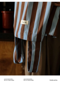 Close-up of striped kitchen apron featuring a Be Original label and premium fabric detail