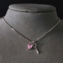 Close-up of a silver necklace featuring a pink heart zircon and a hollow key pendant