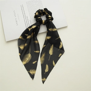 Detail of a black chiffon hair scrunchie with golden feather print and long flowing ribbon
