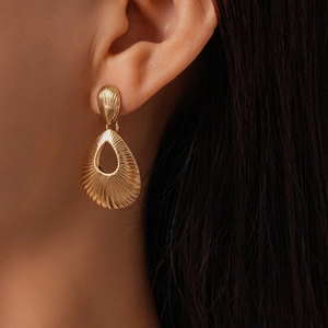 Close-up of gold hollow teardrop earrings with radial texture on a female model