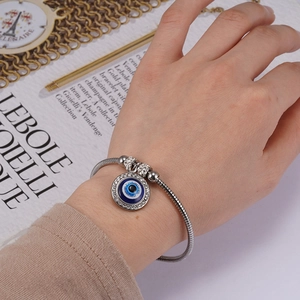 Silver snake chain bracelet with sparkling evil eye pendant worn on a woman's wrist