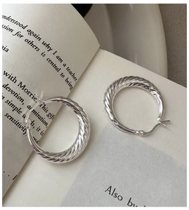 Makroaufnahme von S925 Sterlingsilber gedrehten Creolen auf einer offenen Buchseite