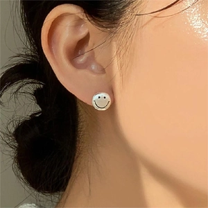 Close-up of a smiling face silver stud earring worn by a model for a minimalist look