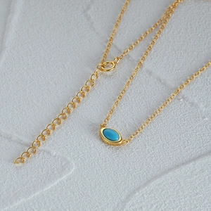 Close-up of golden necklace featuring a turquoise pendant and heart-shaped extender links
