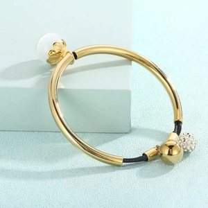 Detail of gold metal tube bracelet with white opal stone and black braided cord