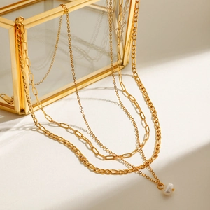 Detail of layered gold-plated necklaces with a white pearl pendant on a glass jewelry box
