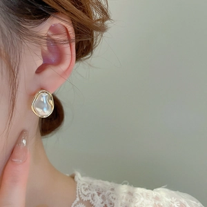 Close-up of elegant irregular baroque pearl earring with a gold frame on a female model