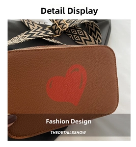 Detail of brown litchi pattern leather bag with red heart and woven geometric strap