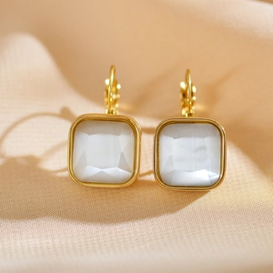 Macro detail of gold-plated square lever-back earrings with white opal stones