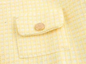 Detail of light yellow tweed fabric with a gold metal button on a jacket pocket